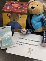 Photo showing Boulder the Bear plush wearing removable blue vest and plaid sleeves, Candy Crave scented sachet packet, themed box, and a note describing the item.