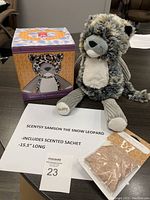 Full lot photo showing Samson the Snow Leopard plush sitting next to the Baked Apple Pie scented sachet and the themed box on table.