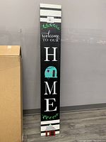 Full view of tall wood plank sign showing entire 'Welcome To Our Home' message with camper cutout as 'O'.