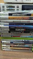 Stacked Xbox 360 game cases showing titles including Grand Theft Auto IV, Assassin's Creed III, Destiny, Far Cry 4, Battlefield 3, Madden NFL 25 among others