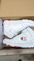 Side view of white Champion sneakers inside box showing logo and condition