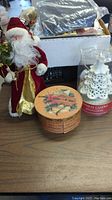 Photo of a Santa Claus figurine in red, a decorative round Christmas box, and part of a Yankee Candle Christmas tree candle.