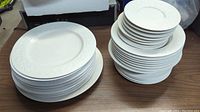 Stack of larger and smaller white embossed pattern plates arranged on a wooden surface.