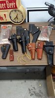 Overview of the lot showing 9 holsters and 2 ammo holders in various styles and materials laid out on a surface.