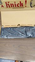 Keyboard wrapped in plastic inside cardboard box on wooden desk