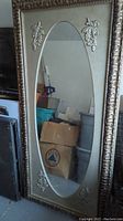 Full view of the large rectangular mirror with an oval reflective surface, showing the carved floral details and frame texture.
