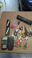 Photo showing assortment of office tools on wood table, including calculator, scissors, rulers, stapler, and hole punch