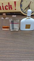 Three perfume bottles: Chanel Allure, Burberry London, and Tom Ford White Patchouli displayed on wooden surface with a partial view of a clock in the background