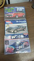 Three sealed plastic model kits stacked on a wooden surface. Top box labeled '69 Shelby GT-500 2 in 1, middle box '78 Corvette Indy Pace Car, bottom box Jeff Gordon No. 24 NASCAR race car.