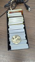 Stack of approximately 500 Pokemon cards in a black storage box with a Pokemon coin on top showing a design.