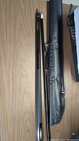 Two-piece black pool cue stick with carrying case laid on wood surface