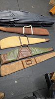 Five rifle cases laid out on the floor, including three soft fabric or leather cases and two hard plastic cases.