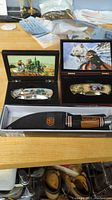 Display showing two folding pocket knives and one fixed blade knife in packaging and sheath.