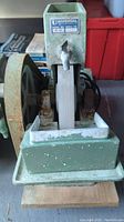 Front view of the Universal Model AE 100 wet stone sander showing the green metal body, water trough with spout, and the grinding wheel.