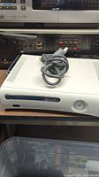 Front view of white Xbox 360 console showing front panel, disc drive, and power button with a cable placed on top.