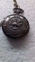 Front of pocket watch showing embossed firefighter helmet and equipment on cover with the words 'FIRE FIGHTER'.