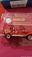 Photo of the 1929 Chevrolet fire truck ornament in plastic packaging showing detailed red fire truck with ladders and decorative elements.