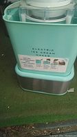 Electric ice cream maker in turquoise plastic and stainless steel base showing front with branding.