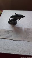 Photo showing the dolphin stone carving and three accompanying certificates including a COA, placed on a white surface.