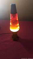 Photo showing the lava lamp glowing with orange and yellow wax inside a clear liquid and plugged in