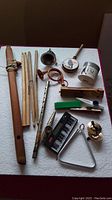 Photo of various musical instruments including wooden flute, drumsticks, piccolo, kazoo, harmonica and others laid out on a white surface.