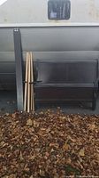 Disassembled dark wood sleigh bed components including headboard, footboard, rails, and slats leaning against a trailer with fallen leaves around
