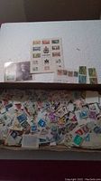 Photo showing a large assortment of loose stamps, some attached to sheets, including a prominent Canada commemorative stamp sheet.
