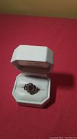 Front view of sterling silver ring in white ring box on red surface