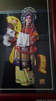 Close-up of Concubine Yang figure in colorful traditional costume holding a fan inside the shadow box frame.