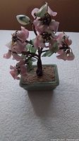 Full view of vintage glass flower tree showing pink glass flowers, green leaves, brown stems, and green square ceramic pot with brown filler.