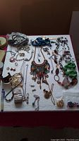 Full display of vintage jewelry lot on white fabric surface, showing necklaces, bracelets, earrings and a large artistic pendant.