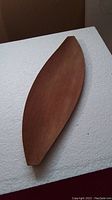 Photo showing full view of the elongated, leaf/boat shaped teak serving tray on a white surface.