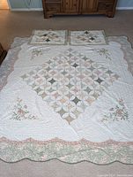 Full view of the queen size quilted bedspread with floral embroidery and scalloped edges, accompanied by two matching pillow shams.
