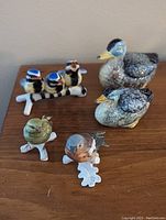 Five bird and duck figurines arranged on a wooden surface, showing front and top details of each bird including the ducks and trio of blue birds on branch.