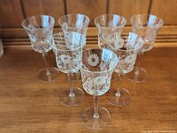 Set of seven clear crystal claret wine glasses with floral etching, arranged together on a wooden surface showing full view of all glasses.