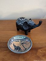 Black elephant figurine with intricate white designs and a small South Africa souvenir plate featuring elephant and bird motifs on a wooden surface.