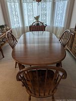 Dining table with four chairs placed around it under natural lighting in a dining room with lace curtains.