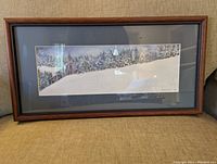 Photo of a framed winter landscape print showing snow-covered hills and trees, wooden frame, and dark matting.