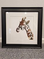 Full frontal view of the framed gold giraffe print artwork against a wall, showing the entire piece with black frame and white matting.