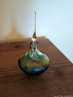 Handblown iridescent glass perfume bottle with tall clear glass stopper on wooden surface