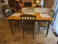 View of kitchen table and 4 chairs showing the green painted legs and backs and natural wood table top with placemats on top