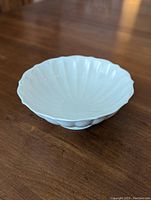 Front angle view of the Lenox scalloped cream-colored bowl sitting on a wooden surface.