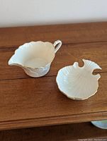 Photo showing the Lenox porcelain creamer and Aegean bowl side by side on a wooden surface, highlighting their shape and gold trim.