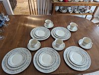 Overview of all five place settings on wood table, showing plates, cups, and saucers arranged neatly with their coordinating patterns and trims.