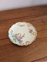 Top view of the Limoges dish showing scalloped edges, pink rose flowers, and gold ornate detailing on cream background.