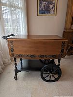 Front view of tea cart with drop leaves closed, showing floral edge decoration and spoked wheels.