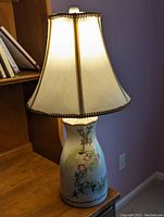 Porcelain lamp on wooden surface with lampshade lit, showing painted floral design