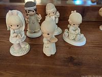 Photo showing five Precious Moments figurines placed on a wooden surface with visible details.