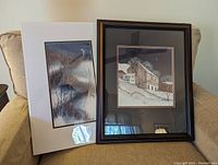 Two art prints on a chair; right print titled 'Night Watch' is framed in dark wood with double mat, left print is double matted and unframed.