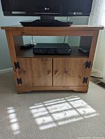 Solid wood TV stand with carved doors, black hinges, and knobs, LG flat-screen TV on top and DVD player on shelf.